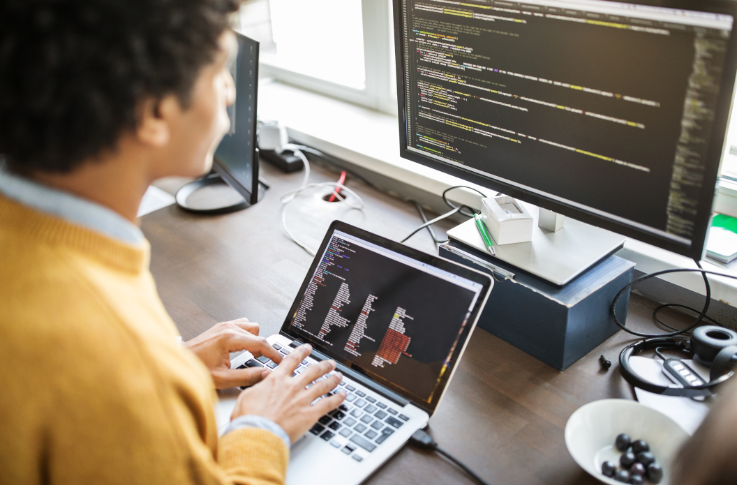 Man looking at two computer screens with code 