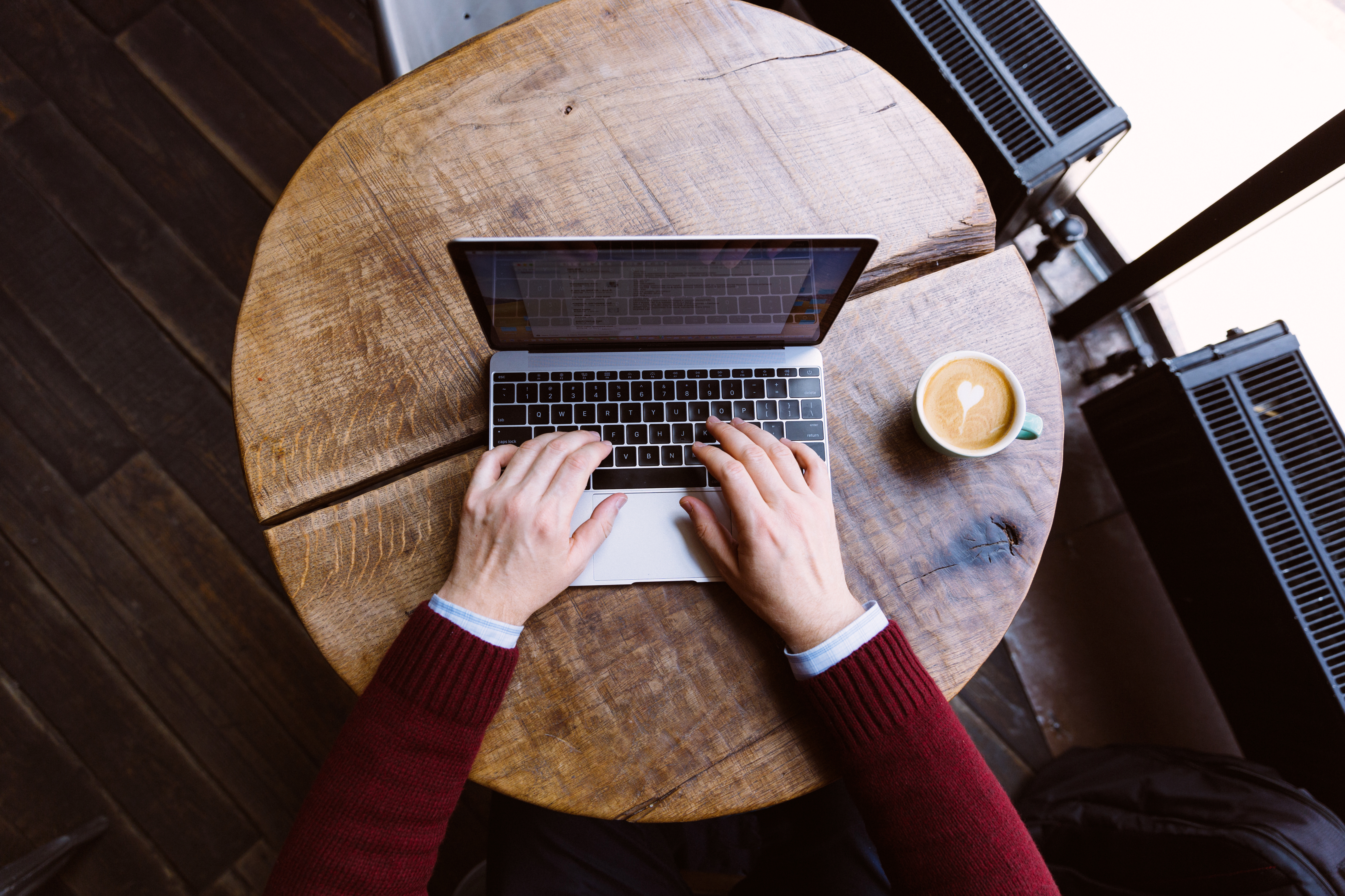 Typing on laptop with coffee next to it in a cafe