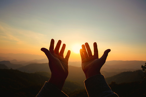 Hands raised to a sunrise sky