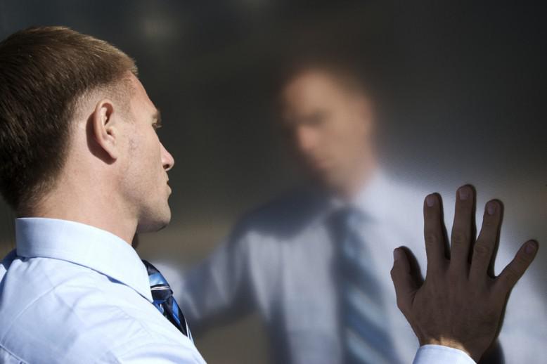 A man looking at his reflection with hands touching the mirror