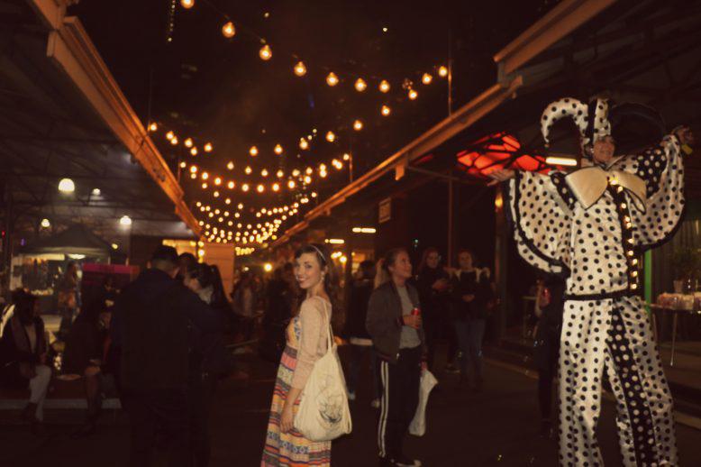 Kaitlyn stands in the middle of a busy Melbourne marketplace at night 