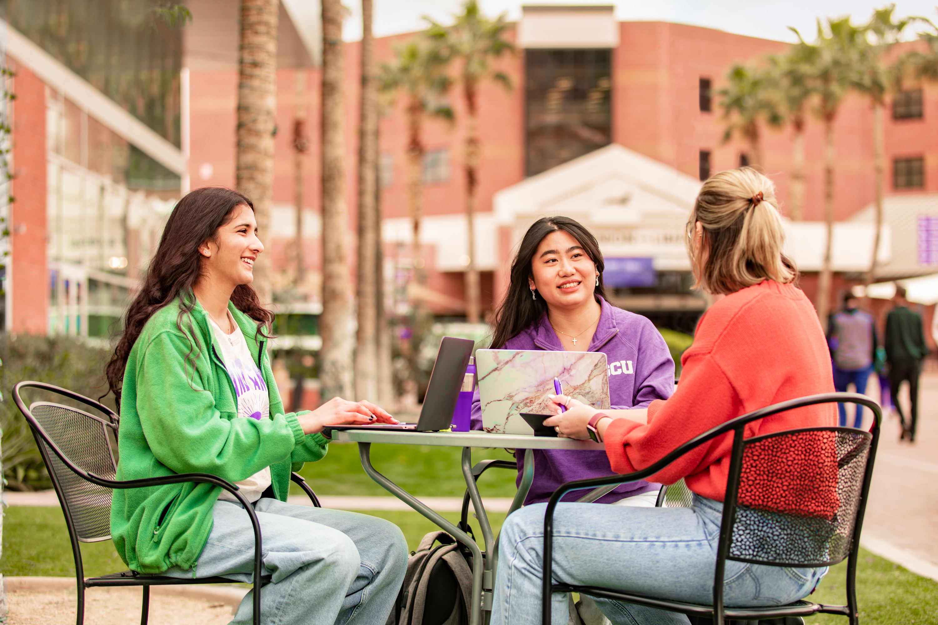 three students sitting at a table on campus