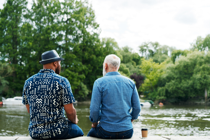 Two men talking, sat next to river