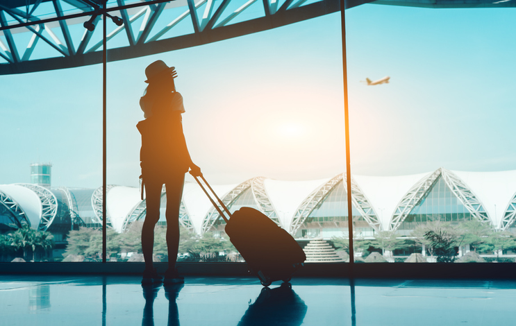 Woman with luggage looking out the window at an airport