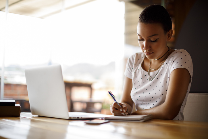 a student taking notes for a class while working on her laptop