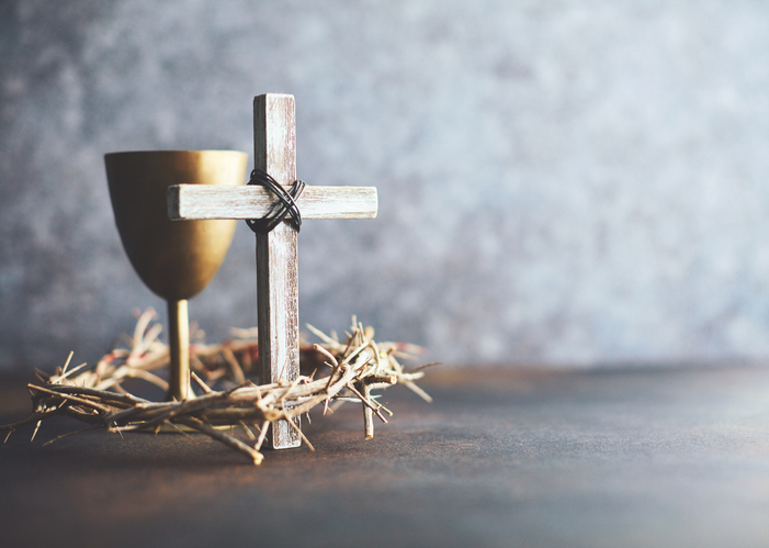 A cross sits with a wine glass and crown