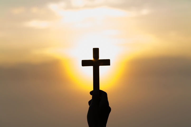 Man holding a cross in front of a sunset