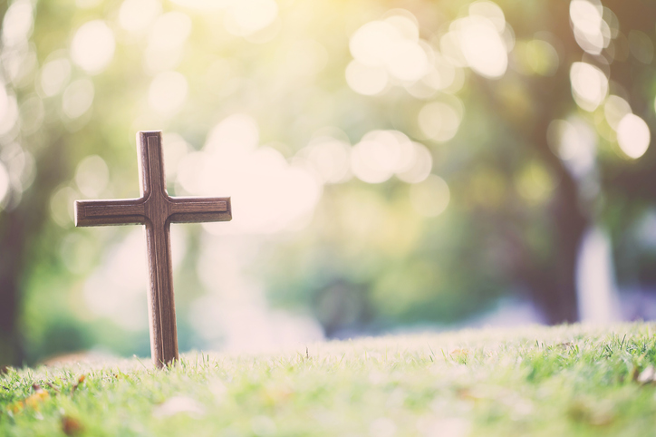 A cross stands alone in an empty grass field
