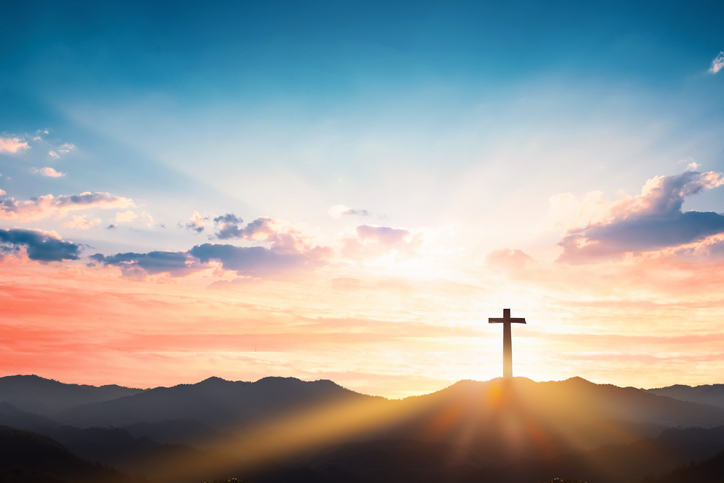 A cross stands in front of behind a beautiful sunset 