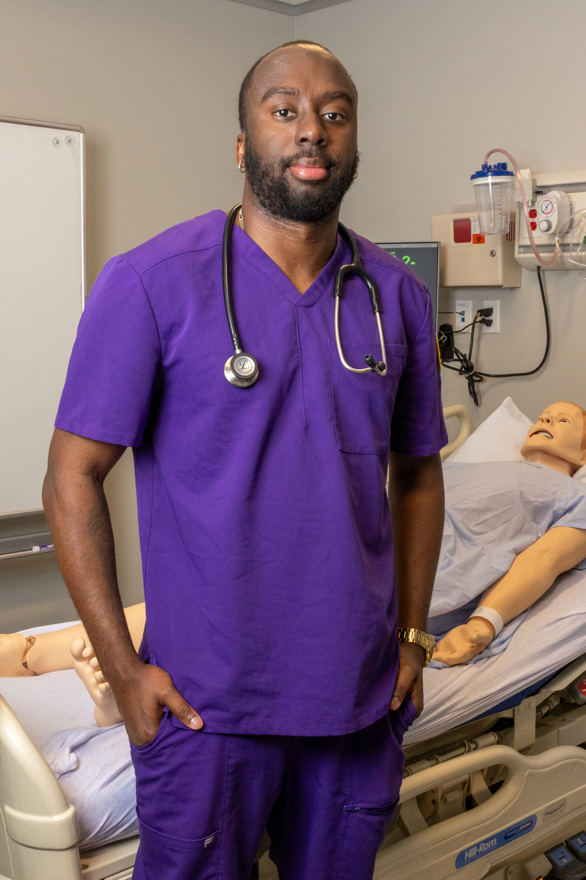 Male nursing student smiling in front of dummy patient in hospital