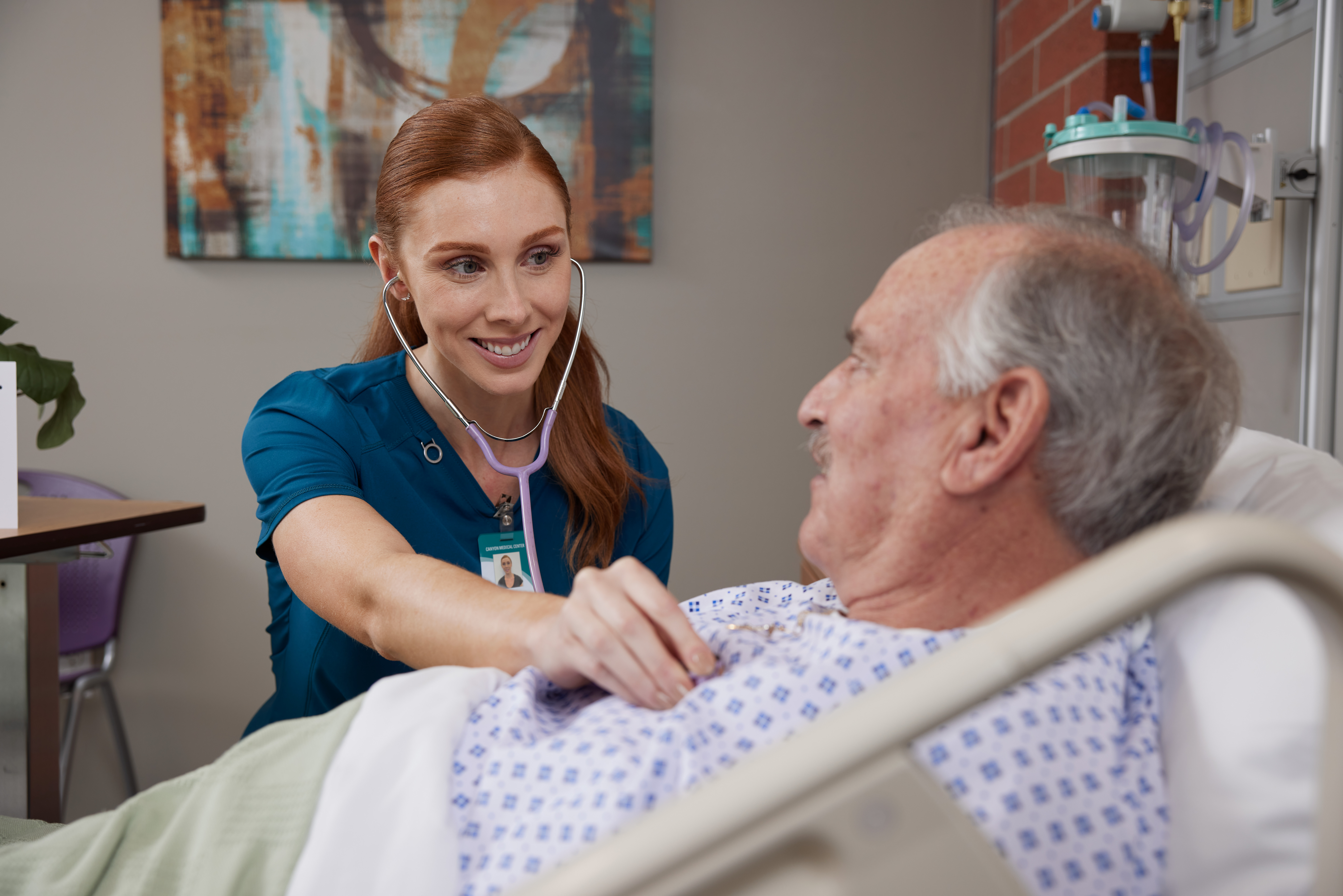 Female nurse taking heartbeat of male patient laying in hospital bed