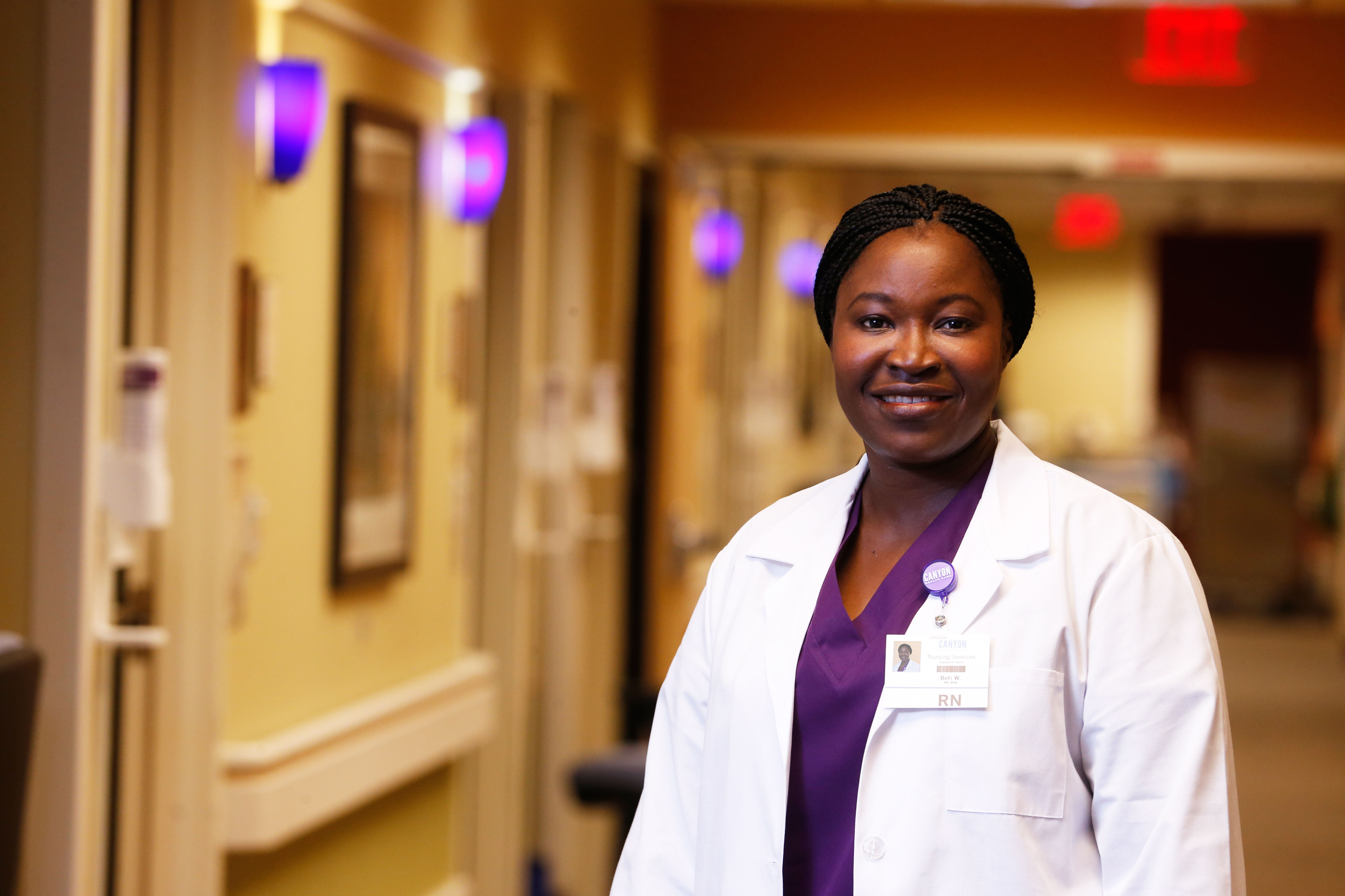 Female DNP degree student at GCU smiling in white lab coat in hospital hallway